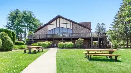Exterior view of the main clubhouse with Tudor-style architecture, wraparound deck, and picnic tables on the lawn.