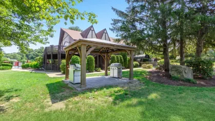 Outdoor grilling area with covered pavilion, stainless steel gas grills, and surrounding greenery near the clubhouse.