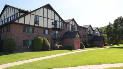 Side view of red-brick apartment buildings with Tudor-style accents, manicured lawns, and trimmed hedges.