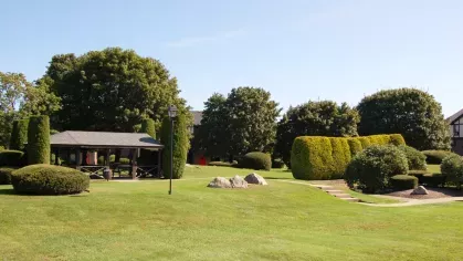 Landscaped courtyard with gazebo, shaped hedges, and stone pathway under clear blue skies.