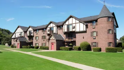 Tudor-inspired apartment exterior with castle-like turret, red doors, and neatly edged lawns.