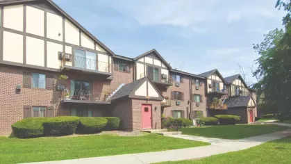 Row of apartment homes featuring Tudor-style gables, small patios, and lush green landscaping.