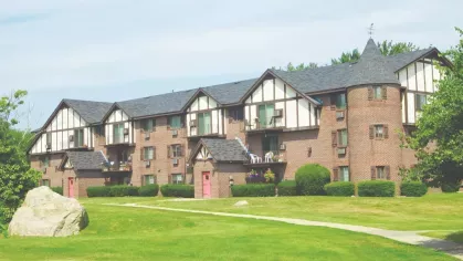 Red-brick apartment building with turret design and Tudor-style trim surrounded by expansive green space.