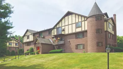 Tudor-style brick apartment building with turret and balconies surrounded by manicured lawns and mature trees.
