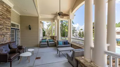 Covered area near the swimming pool with chairs, tables, and a ceiling fan. 
