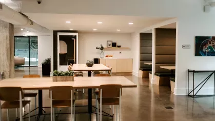 A stylish lounge area at Industry Columbus Apartments featuring modern brown leather chairs, a pool table, and a staircase with built-in seating beneath an industrial-style ceiling.