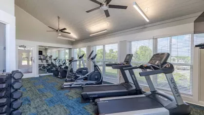 Fitness center with multiple fitness machines and overhead lights and ceiling fans. 