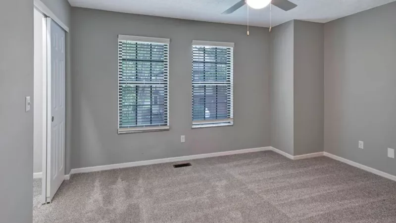 Large, open bedroom with bright overhead lighting and ceiling fan.