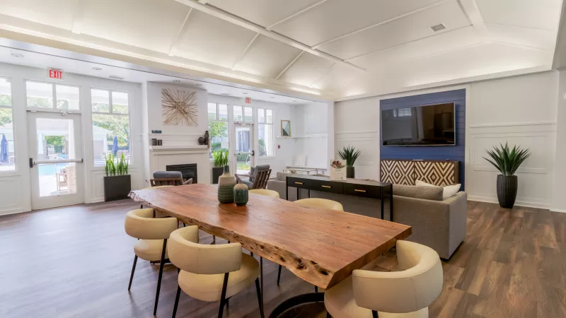 Spacious modern communal room with a live-edge wooden table and cream chairs, plus a lounge area with a sofa and TV.