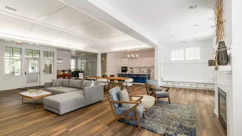 Spacious open-plan living room with grey sectional, armchairs, and a modern kitchen with a blue island in the background.