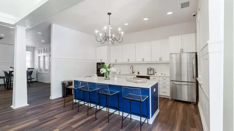 Modern kitchen with a blue island, white cabinets, stainless steel refrigerator, and dark wood floors.