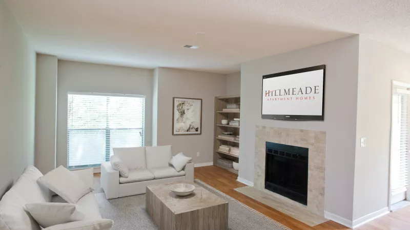 Bright living room with two white sofas, coffee table, fireplace, and TV displaying InterMeade Apartments logo.