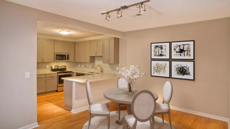 Modern dining area with a round table, four chairs, and abstract wall art, open to a kitchen with light cabinets and an island.