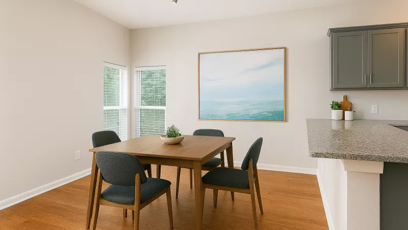 Modern dining area with a wooden table, four dark chairs, landscape art, and a kitchen counter with gray cabinets.