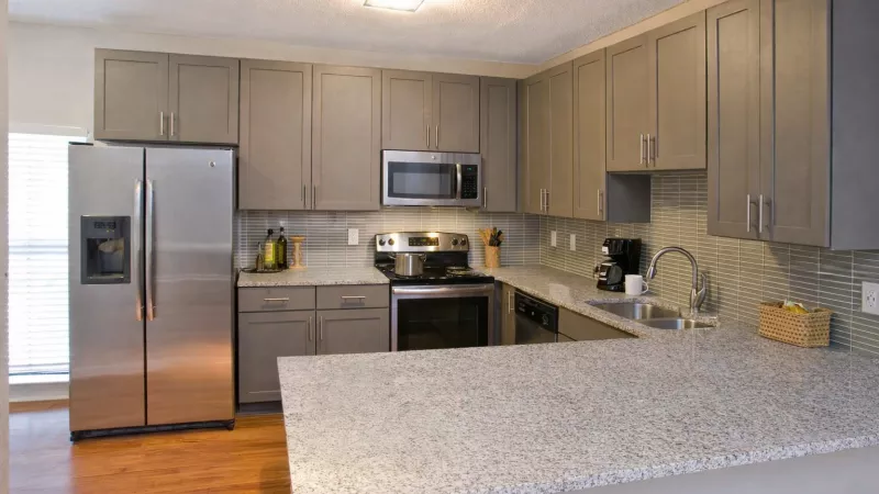 Modern kitchen with gray cabinets, granite countertops, stainless steel appliances, and a light wood floor.