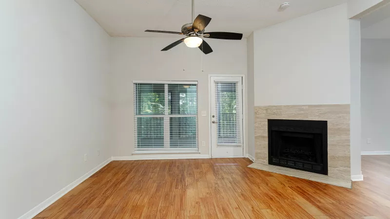 Bright living room with wood floors, white walls, a ceiling fan, large windows, and a corner stone fireplace.