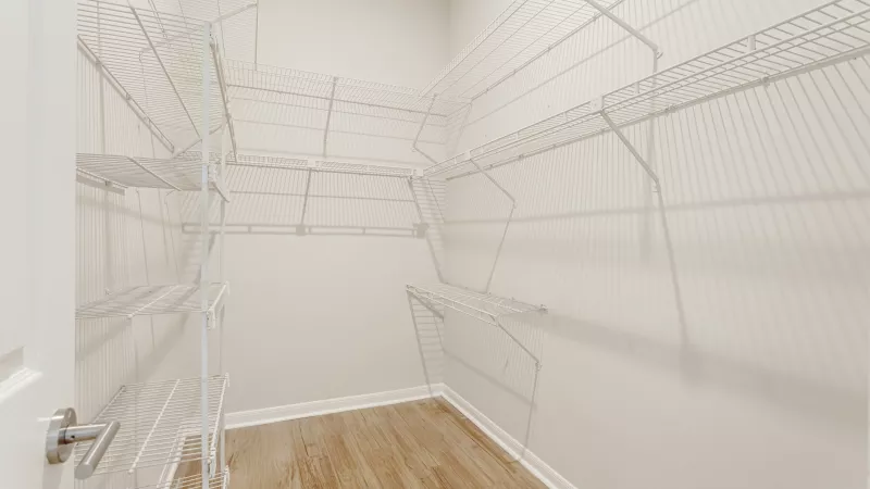 Spacious, empty walk-in closet with white wire shelving on walls and light wood floor.