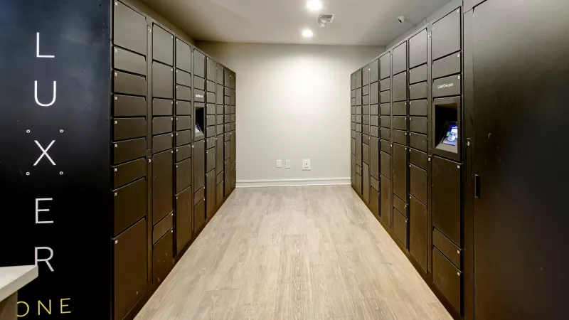 Long hallway lined with dark brown package lockers. A black panel on the left reads "LUXER ONE" vertically.