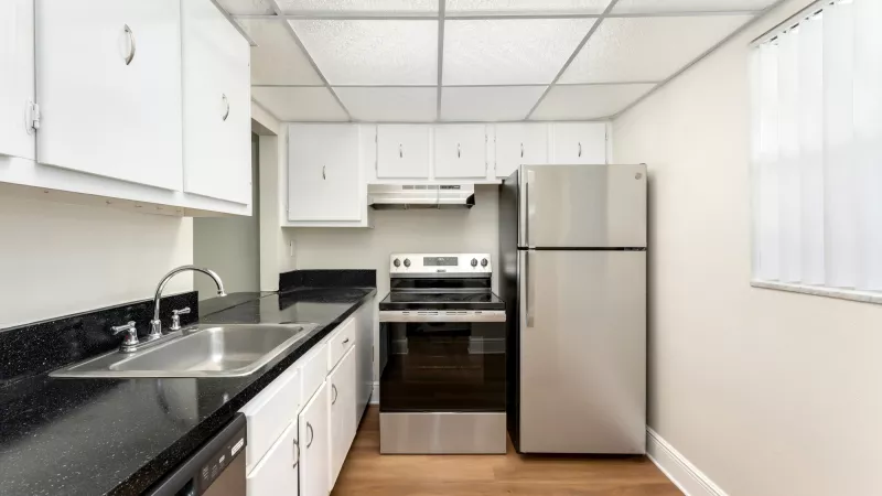 Small kitchen with white cabinets, black countertops, stainless steel refrigerator and range, and wood-look floor.