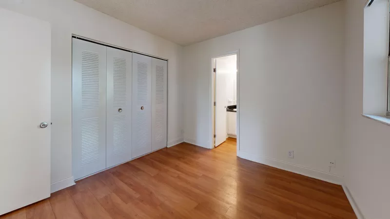 Empty room with hardwood floor, white walls, bi-fold closet, door, and a doorway to a bathroom.