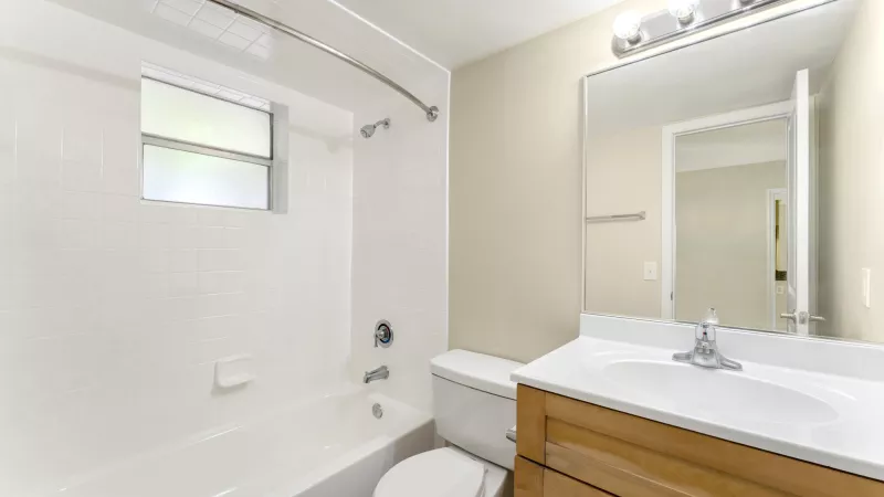Clean small bathroom with white tub, toilet, light wood vanity, sink, and mirror.