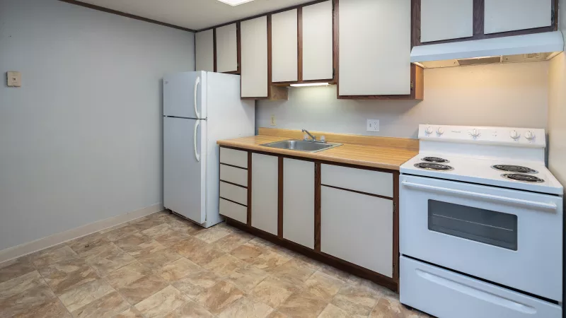 Compact kitchen with white refrigerator and stove, light countertops, white and brown cabinets, and brown patterned floor.