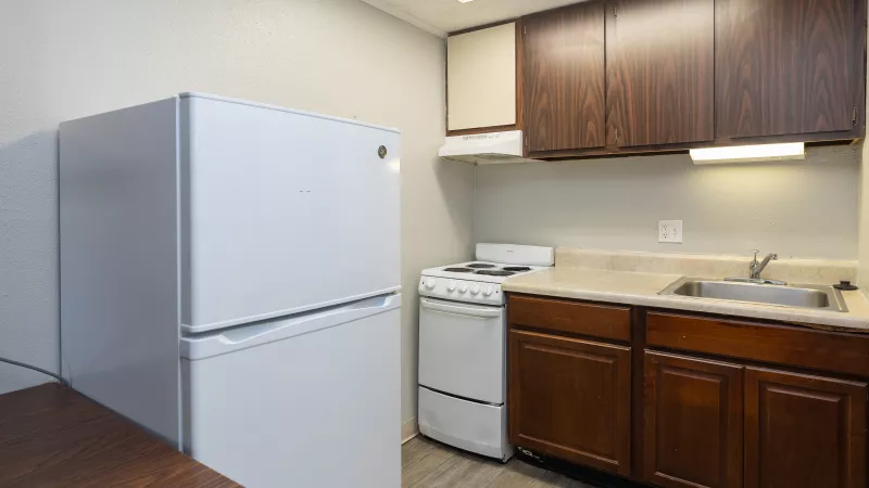 Small kitchen with a white refrigerator, stove, dark wood cabinets, light countertop with a sink, and a wooden floor.