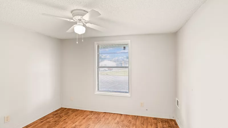 Unfurnished bedroom with light gray walls, wood laminate flooring, a white ceiling fan, and a window with blinds.