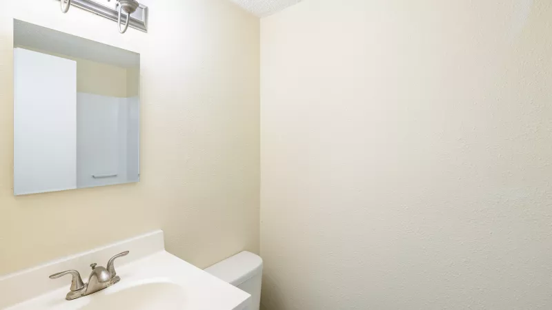 Small bathroom with a white vanity, sink, mirror, light fixture, and toilet. Light yellow walls are visible.