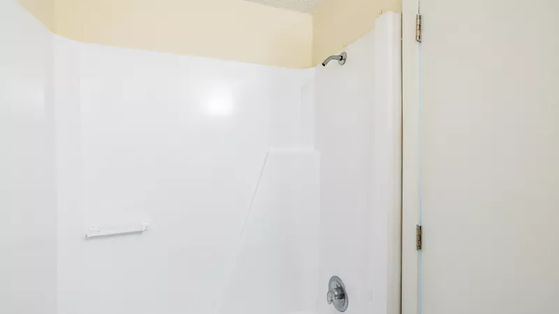 White shower stall with a chrome showerhead and faucet, set against light yellow bathroom walls.