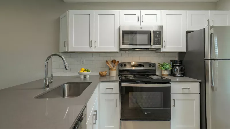 Clean, modern kitchen with white cabinets, gray countertops, stainless steel microwave, stove, and refrigerator.