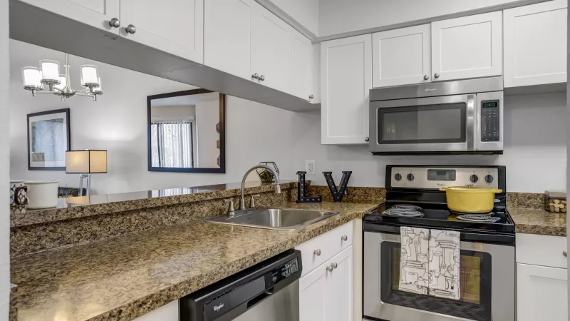 Kitchen with white cabinetry, speckled granite countertops, and stainless steel appliances. A yellow pot sits on the stove.