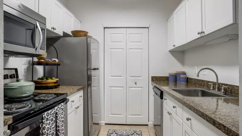 Narrow kitchen with white cabinets, speckled granite counters, stainless steel appliances, and a decorative rug.