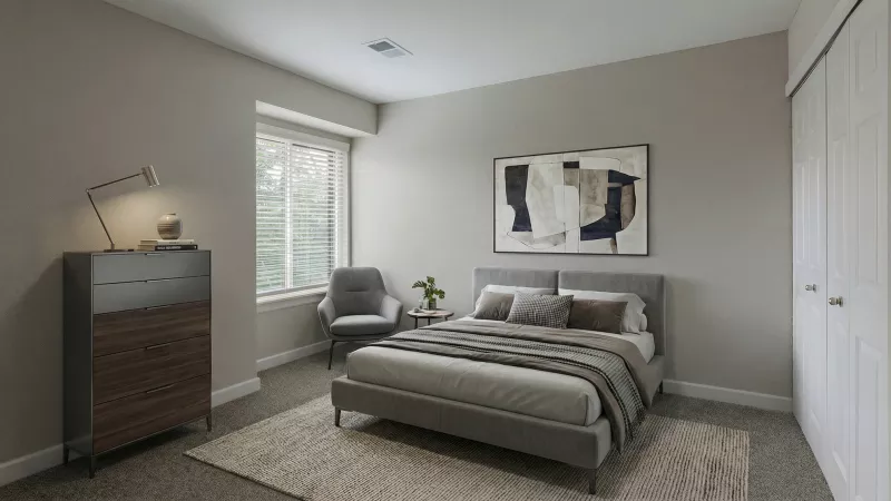 Modern bedroom with a gray bed, abstract art, tall dresser, and an armchair by the window.
