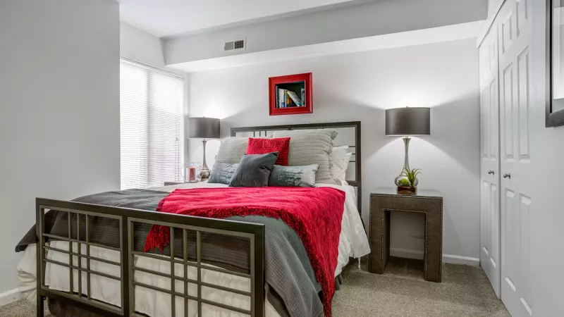 Contemporary bedroom with a bed, red and gray bedding, lamps on nightstands, a red framed picture, and window.