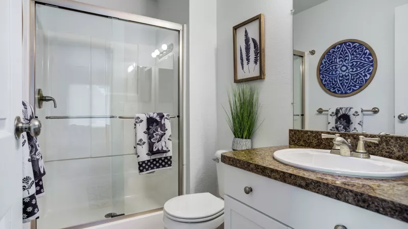 Modern bathroom featuring a glass shower, white toilet, vanity with a speckled countertop and sink, plus blue accents.
