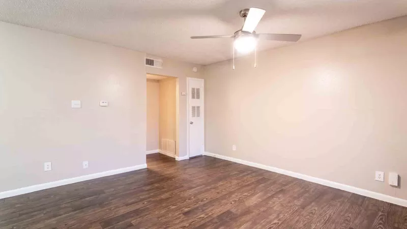 Empty room with light beige walls, dark wood floor, ceiling fan, and a doorway to another area with a built-in cabinet.