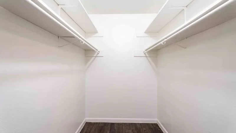 White walk-in closet with dark wood flooring and empty white shelves on both sides.