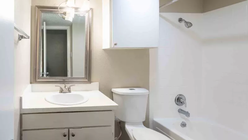 Clean, small bathroom with white vanity, mirror, toilet, and bathtub with shower.