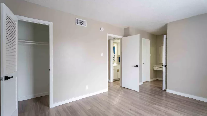 Empty room with light walls, wood-look floor, an open closet, and a bathroom visible through an open door.