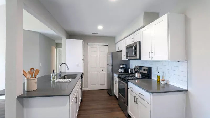 Modern kitchen with white shaker cabinets, dark gray countertops, stainless steel appliances, and a tiled backsplash.
