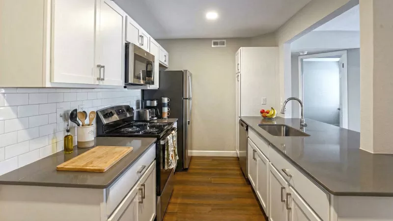 Bright, modern kitchen with white cabinets, dark gray countertops, stainless steel appliances, and hardwood floors.