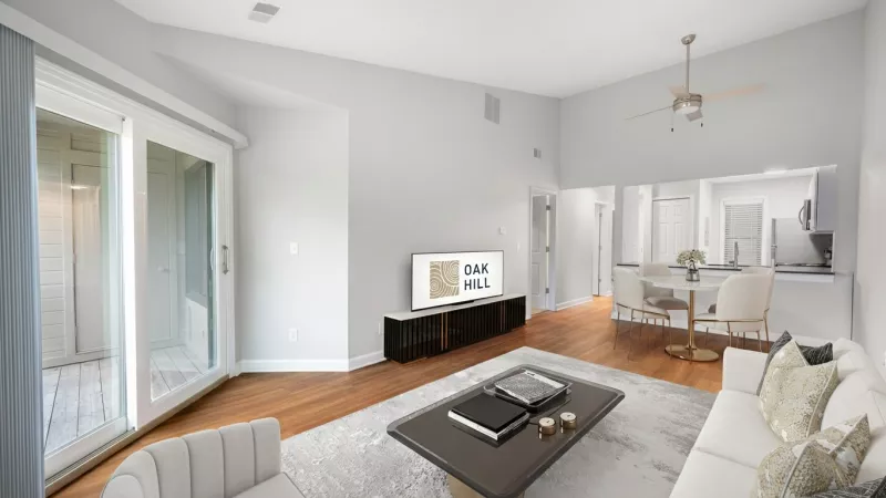 Bright living room with white sofa, coffee table, and TV. Sliding door to balcony, kitchen and dining area in background.