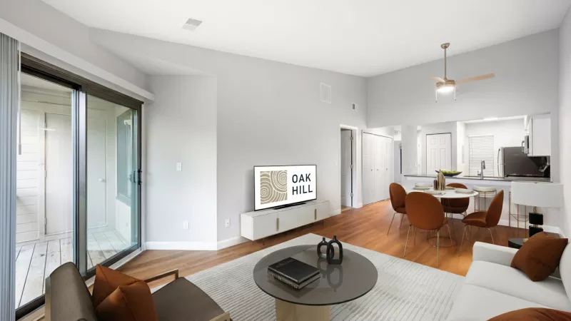 Modern open-concept living room with white sofa, dining area with orange chairs, and a kitchen. Balcony access.