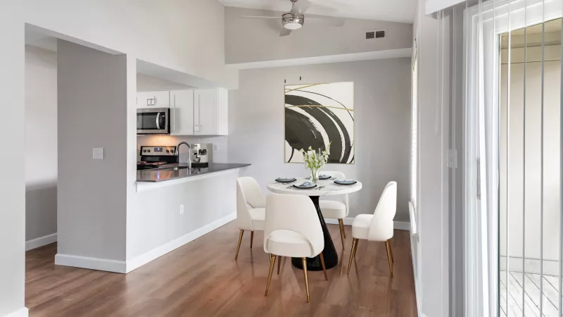 Modern kitchen with white cabinets, dark counters, open to a dining area with a round white table, four chairs, abstract art, and wood floor.