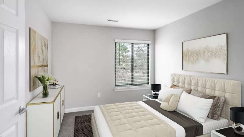 Modern bedroom with a beige bed, white dresser with gold accents, and a window with a treed view.