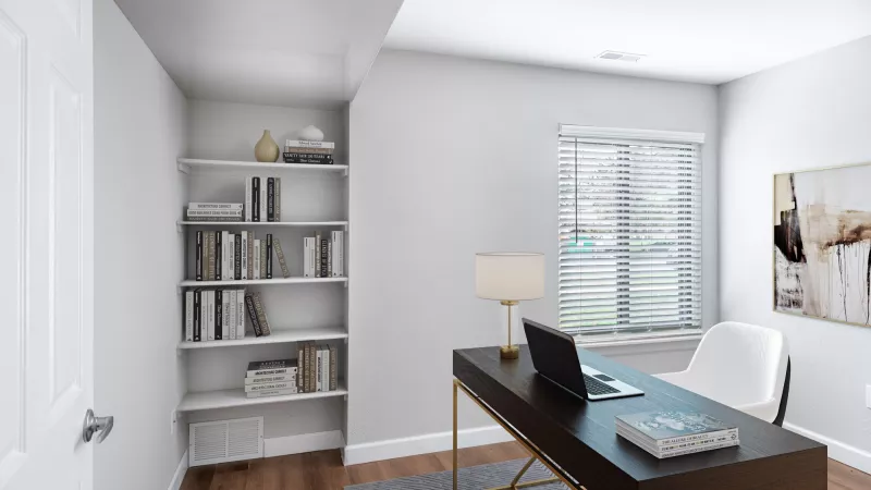 Bright home office with a dark desk, laptop, white chair, built-in white bookshelf, and window with blinds.