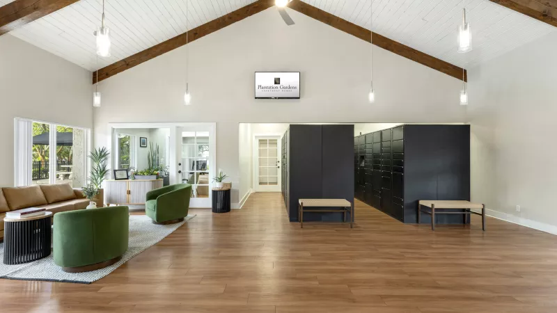 Spacious modern lobby with vaulted ceiling, seating area with green chairs, and dark mailboxes with benches.