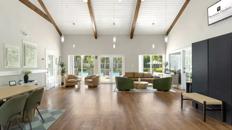 Spacious clubhouse lounge with vaulted ceiling, wood floors, and view of an outdoor pool. Features Signature Living logo.