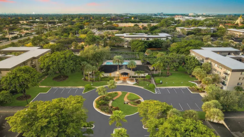 Aerial view of a sprawling resort complex featuring a circular drive, lush greenery, buildings, and a vibrant pool area at dusk.
